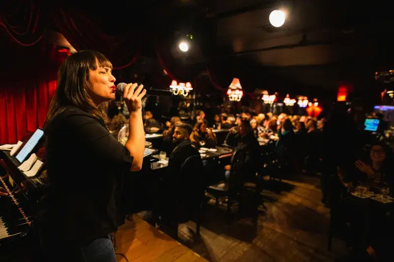A person holds a microphone at  Don’t Tell Mama Piano Bar stage