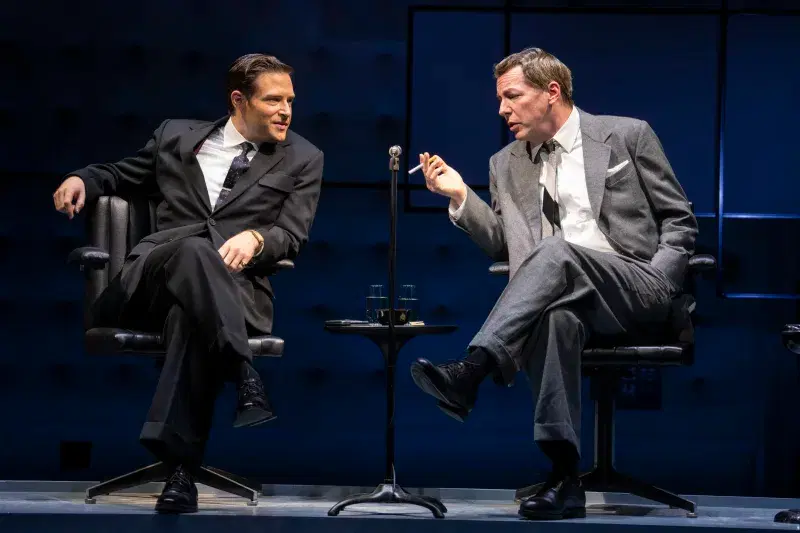 Actors sitting next to each other on chairs while performing on stage