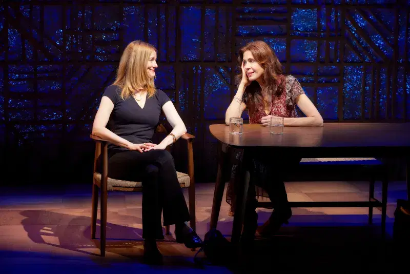 two women sitting at a table talking to each other on stage