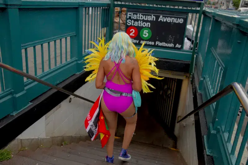 Person in costume with yellow feathers walking down the stairs towards subway entrance