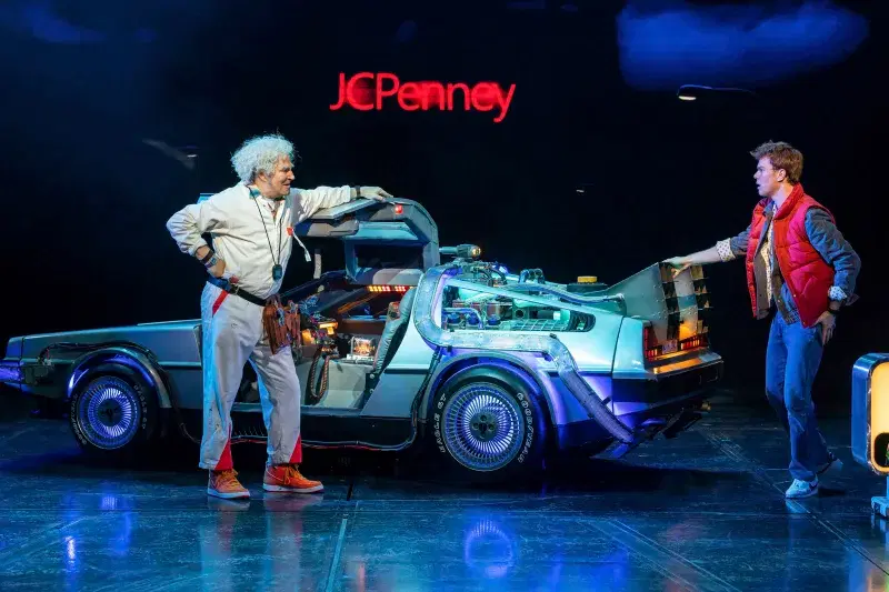 two actors standing next to a car on a stage 